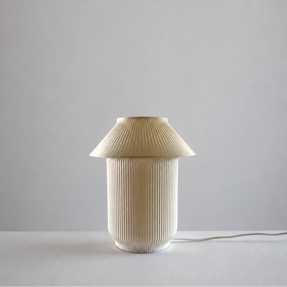 A modern pleated table lamp in a warm cream or beige color, featuring a pleated conical shade and a matching pleated cylindrical base, set against a minimalist light gray background.