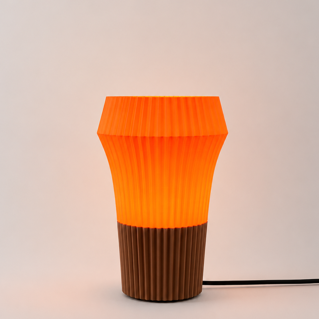 A modern pleated table lamp with a translucent orange upper shade and a ribbed brown base, shown on a light gray background with its power cord visible.