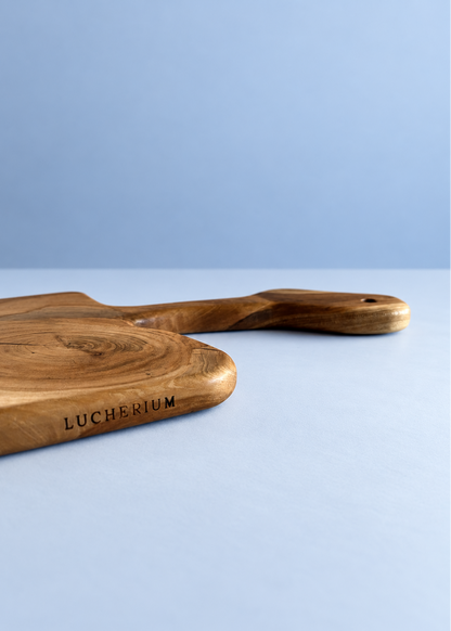 A close-up of a wooden serving board with a handle, featuring the engraved brand name 'LUCHERIUM' on a light blue background.