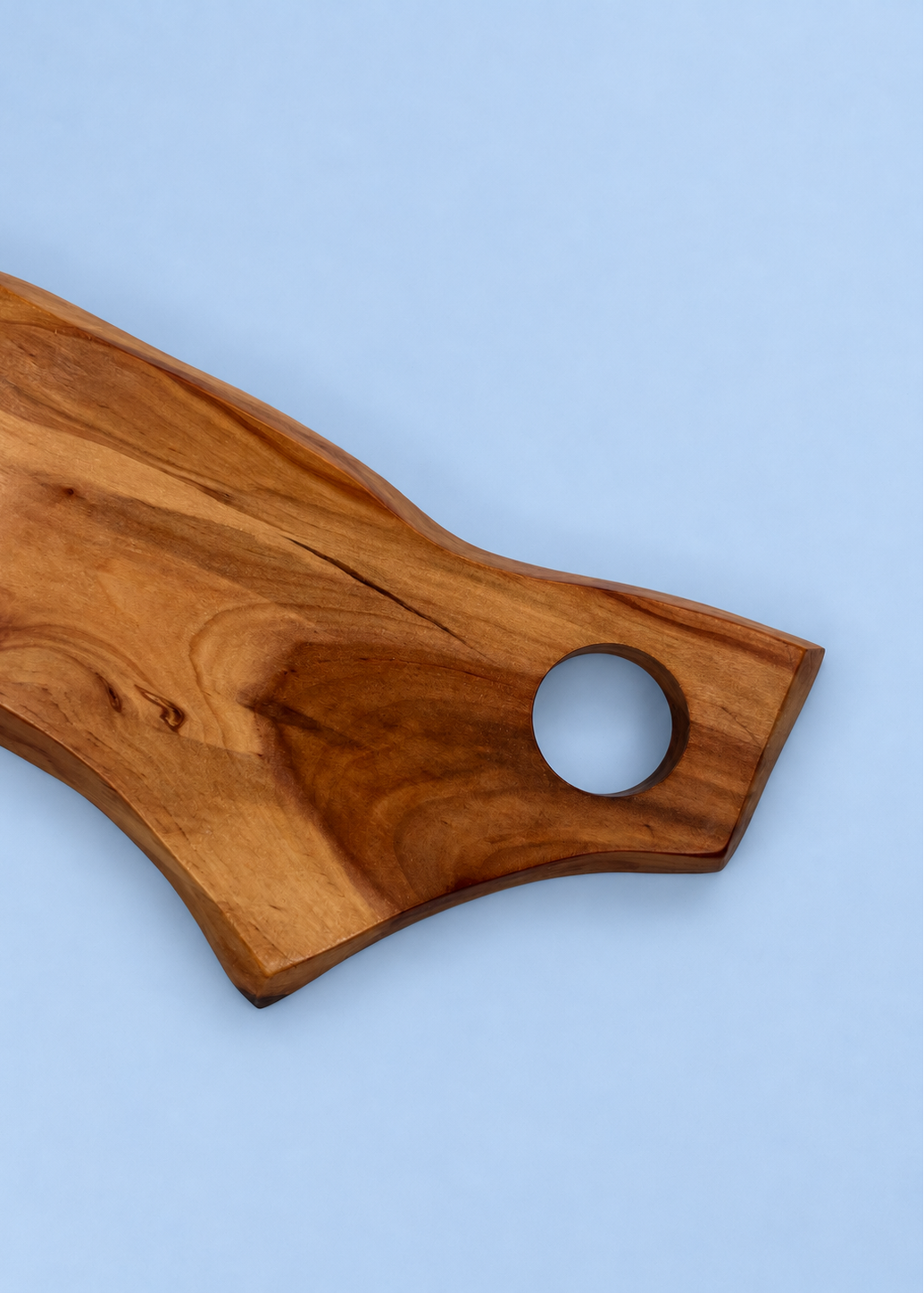 A rustic wooden serving board with a live edge and a circular cutout, shown on a solid light blue background.