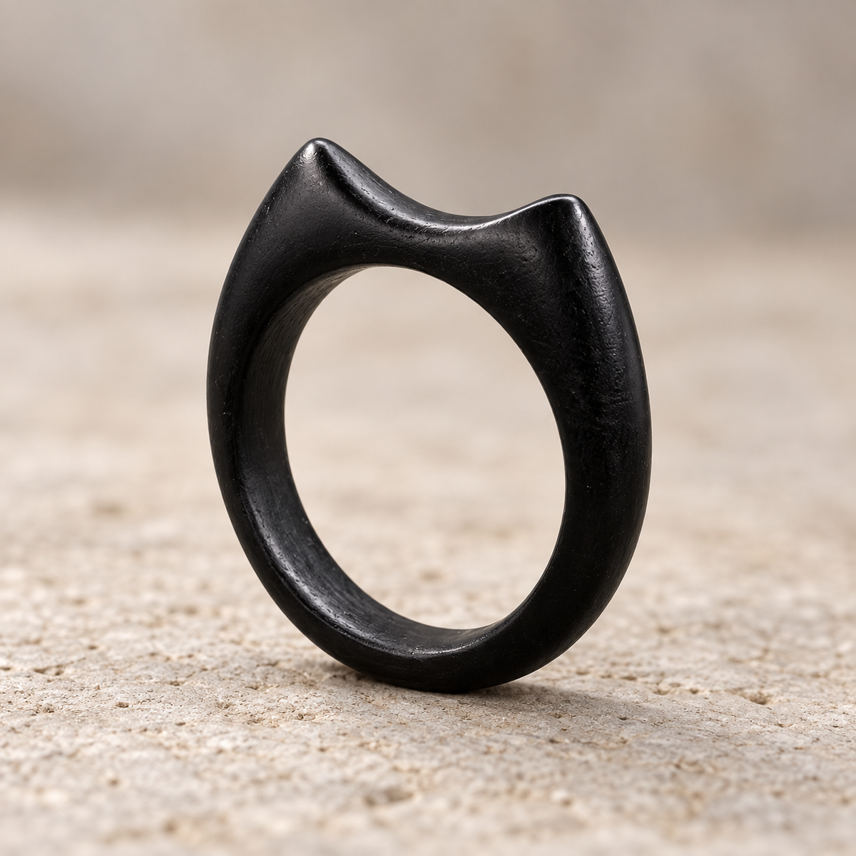 A matte black cat-shaped ring standing upright on a textured sandy surface with a soft beige background.