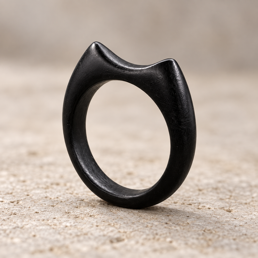A matte black cat-shaped ring standing upright on a textured sandy surface with a soft beige background.